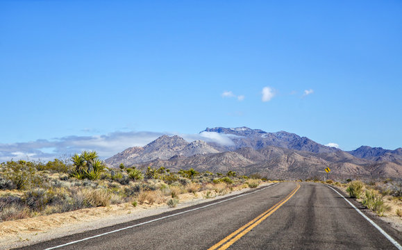 A highway cutting through the Mojave desert with a large mountain in the foreground in a march landscape