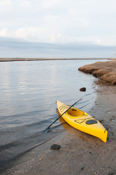 vertical photo of yellow kayak and paddle on a beach.