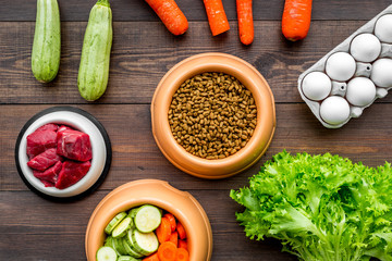 Dry pet food with natural ingredients. Raw meat, vegetables zucchini and carrot near eggs on dark wooden backgroud top view