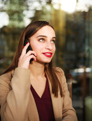 Nice girl in coat uses mobile phone in summer cafe