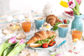 Delicious spring breakfast on a white background. Bouquet of fresh tulips. Small and large colored Easter eggs. Oatmeal, coffee, fresh berries. Postcard for Easter.