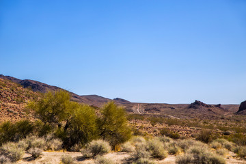 A marrow trail in the distance cutting through the Mojave desert in a march afternoon
