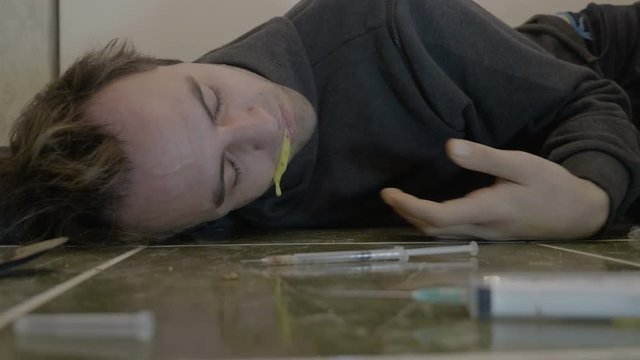 Intoxicated young boy lying on the bathroom floor spasm unconsciously and vomiting after injecting an overdose of heroin drug