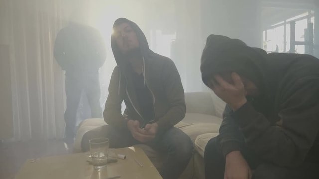 Two narcotic boys in hood sharing a marijuana joint in a smoky room while another man comes from the window and asking for weed
