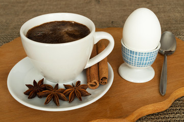 A cup of coffee on a saucer, a tubberry, a cinnamon, an egg on a stand