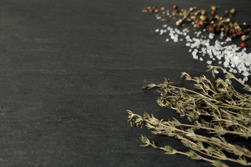 Coarse salt crystals, peppercorns and thyme on dark slate background - low angle, selective focus,...