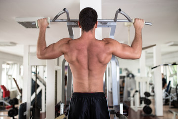 Young attractive adult man exercising and doing weight lifting at fitness gym. Sport training indoors.