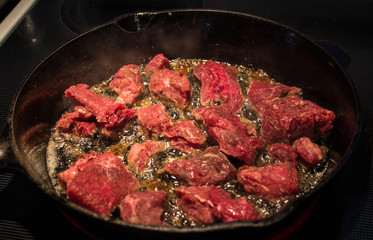 Beef Cooking and Sizzling in Cast Iron Frying Pan on Stove
