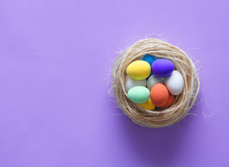Mini colorful eggs in a nest on blue paper background. Happy Easter.
