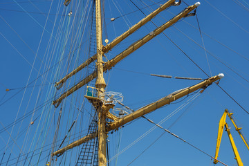 Masts of a sailing ship with the lowered sails with blue sky on the background.