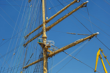 Obraz premium Masts of a sailing ship with the lowered sails with blue sky on the background.