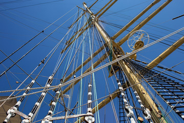 Masts of a sailing ship with the lowered sails with blue sky on the background.