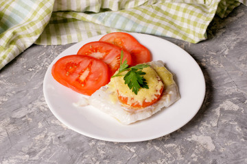 Fish baked with cheese and tomatoes on a white plate