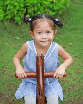 Little child girl riding on a wooden toy horse in the green grass garden.