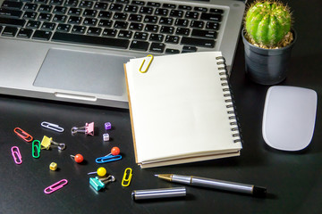 Top view of office table or desk with blank notebook, laptop, colorful equipment and smart phone on black background with copy space for text.