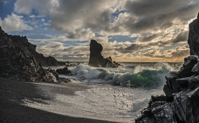 Waves Crash against the Sea Stacks on the Icelandic Beach beach of Dritvik as the Sun Back Lights the Scene