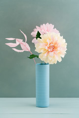 Pink and beige crepe paper dahlias in a vase on turquoise wooden background