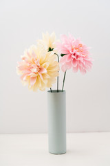 Pink and beige crepe paper dahlias in a vase on white background