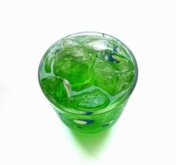 Closeup top view of a glass of green beverage with ice on white background.