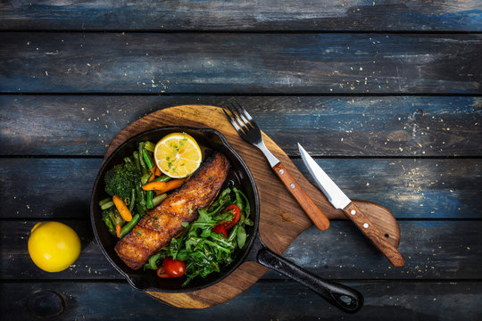 Grilled Salmon Fillet In A Frying Pan, Vegetables, Arugula With A Lemon.