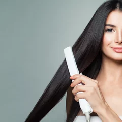 Foto op Canvas Beautiful Woman with Long Straight Hair Using Hair Straightener. Cute Smiling Girl Straightening Healthy Brown Hair with Flat Iron on Gray Background © millaf