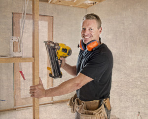  confident constructor carpenter or builder man working wood with electric drill at industrial construction site in installation and renovation work industry