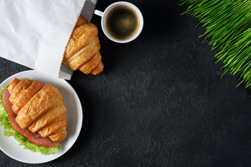 Croissant with ham and lettuce, coffee and sprouted wheat on a dark background. Breakfast flat lay.