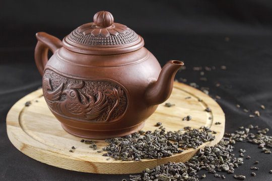 Clay teapot and scattered tea on a wooden stand