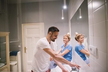 Charming lovely smiling couple in pajamas having a conversation in front of the mirror in the bathroom.