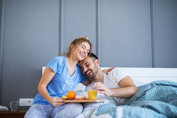 Young smiling couple in love having breakfast together in bed and hugging each other. Relationship and weekend goals.