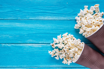 Popcorn in brown paper cups on blue wooden background with copy space, top view, flat lay. Cinema concept.