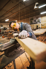 Portrait view of happy attractive hardworking middle aged professional female carpenter worker looking and choosing wood in the workshop or garage.