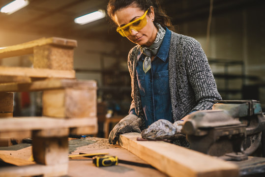 Portrait view of happy attractive hardworking middle aged professional female carpenter worker looking and choosing wood in the workshop or garage. - Powered by Adobe