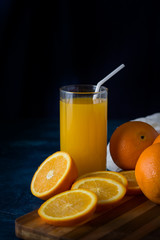 A glass of Fresh Orange Juice with a Tube, Orange slices, Oranges, white Cloth on a Dark Blue Background