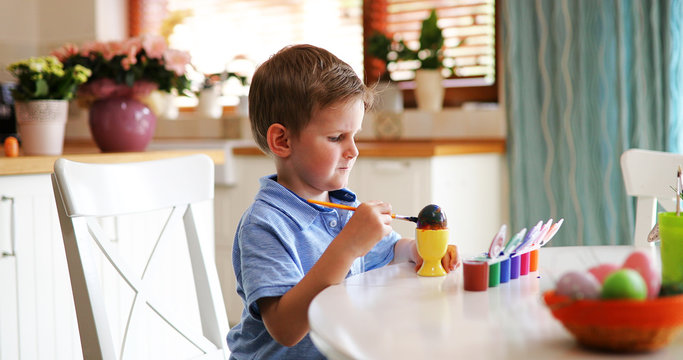 Little kid boy coloring eggs for Easter holiday in domestic kitchen