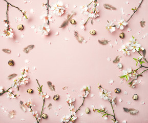 Naklejka premium Easter holiday background. Flat-lay of tender Spring almond blossom flowers on branches, feathers, quail eggs over light pink background, top view, copy space. Greeting card concept