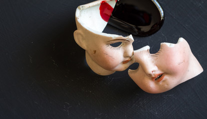 Broken doll faces and blood isolated on grunge black background with blood spatter. Conceptual image of violence against children and women