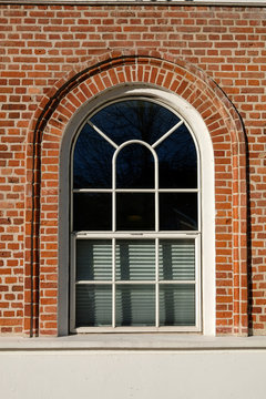 Tall rounded format metal barn style window with designed glazing pattern, in a red brick facade