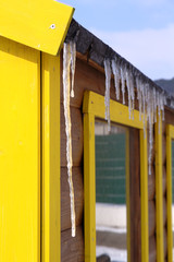 Wintry roof of the house with icicles on blue sky background.