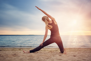 young woman exercising on the beach at beautiful sunset