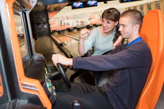 young couple playing driving wheel video game in game room