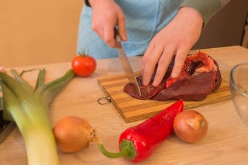 a man in a kitchen apron, meat on a board and a wooden table, a knife and vegetables