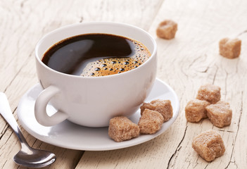 Cup of coffee and brown sugar cubes on the wooden table.