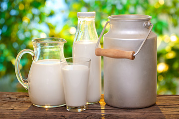 Farm milk in different dishes on the wooden table. Blurred evening nature at the background.