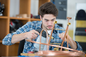 young metalworker holding blowtorch against copper pipe
