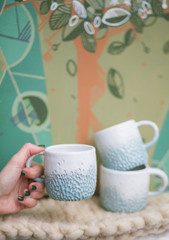 Earthenware crockery. Woman holds white cup with blue sea on the beige cloth