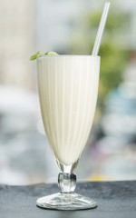 Milkshake in a large glass with a tube decorated with mint. View from above. Background blur