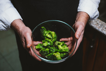 Man of 59 year old  shows  broccoli in the kitchen of his house.