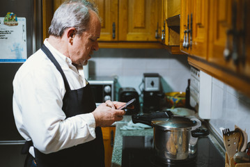 Fototapeta na wymiar Man of 59 year old with smartphone in the kitchen of his house.