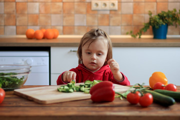 Cute baby girl eating healthy vegetables at kitchen